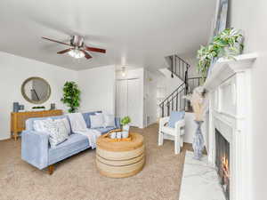 Carpeted living area with stairway, a fireplace, and a ceiling fan