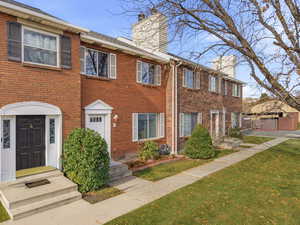 Colonial-style house featuring a chimney, brick siding, and a gate