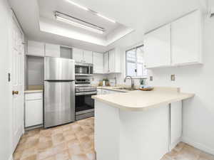 Kitchen with a tray ceiling, light countertops, white cabinetry, appliances with stainless steel finishes, and a peninsula