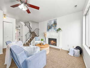 Living area featuring carpet, stairway, a premium fireplace, and a ceiling fan
