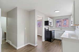 Kitchen with appliances with stainless steel finishes, white cabinetry, light wood-type flooring, and light stone countertops