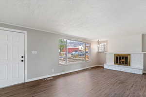 Unfurnished living room with dark wood-style flooring, a fireplace, a textured ceiling, and crown molding