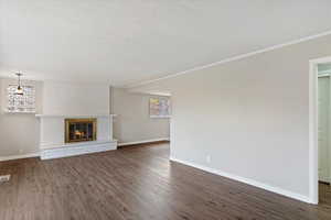 Unfurnished living room featuring a fireplace, a textured ceiling, dark wood-style flooring, and crown molding