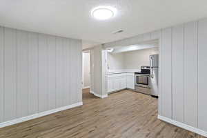 Kitchen with a textured ceiling, light countertops, white cabinets, wooden walls, and light wood-style flooring