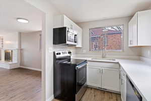 Kitchen featuring appliances with stainless steel finishes, white cabinets, light wood-type flooring, light stone countertops, and a brick fireplace