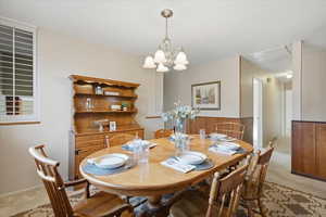 Dining room with light carpet, a chandelier, and attic access
