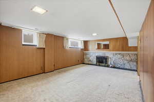 Basement featuring wood walls, a fireplace, and light carpet