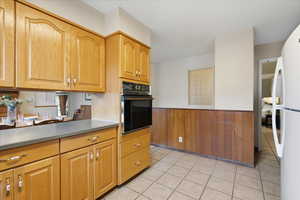 Kitchen featuring a wainscoted wall, black oven, freestanding refrigerator, wood walls, and light tile patterned floors
