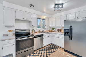 Kitchen featuring stainless steel appliances, white cabinets, light countertops, and light tile patterned flooring
