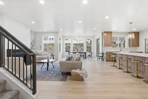 Living area with stairs, a chandelier, plenty of natural light, light wood finished floors, and recessed lighting