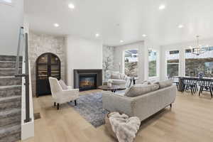 Living area featuring stairs, light wood-type flooring, a chandelier, a glass covered fireplace, and recessed lighting