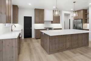 Kitchen with hanging light fixtures, appliances with stainless steel finishes, light stone counters, a kitchen island, and light wood-style floors