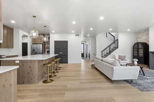 Kitchen featuring light stone counters, pendant lighting, stainless steel appliances, a breakfast bar area, and light wood finished floors