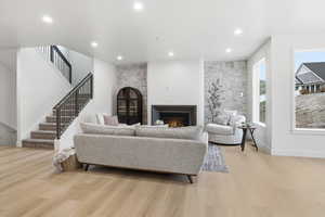 Living room featuring a glass covered fireplace, stairs, light wood-type flooring, and recessed lighting