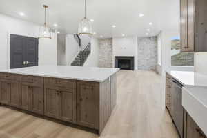Kitchen with a fireplace, light wood finished floors, light stone counters, pendant lighting, and recessed lighting