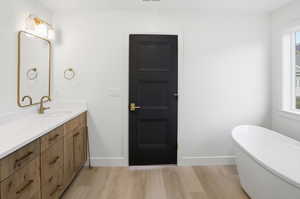 Full bathroom featuring a soaking tub, light wood finished floors, plenty of natural light, and vanity