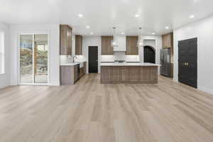 Kitchen with decorative light fixtures, light wood-style floors, a kitchen island, brown cabinets, and recessed lighting
