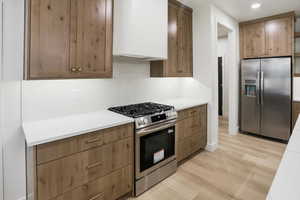 Kitchen with stainless steel appliances, light countertops, light wood-style flooring, decorative backsplash, and open shelves