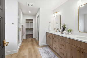 Full bath with double vanity, a walk in closet, light wood-style floors, recessed lighting, and a shower stall