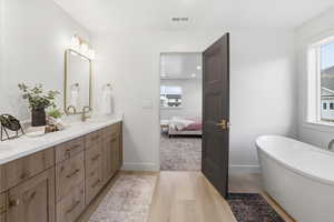 Bathroom with a freestanding tub, double vanity, ensuite bathroom, and light wood finished floors
