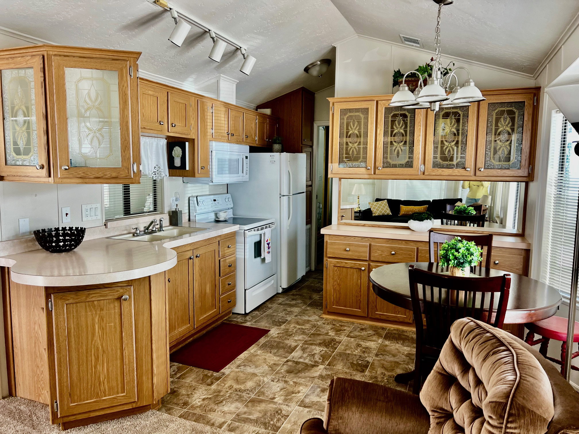 Kitchen featuring glass fronted cabinets, suspended lighting, white appliances, wood finish cabinetry, and light countertops