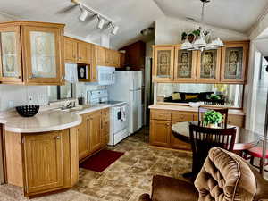 Kitchen featuring glass fronted cabinets, suspended lighting, white appliances, wood finish cabinetry, and light countertops