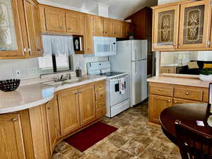 Kitchen with glass fronted cabinets, white appliances, light countertops, and wood finish cabinets