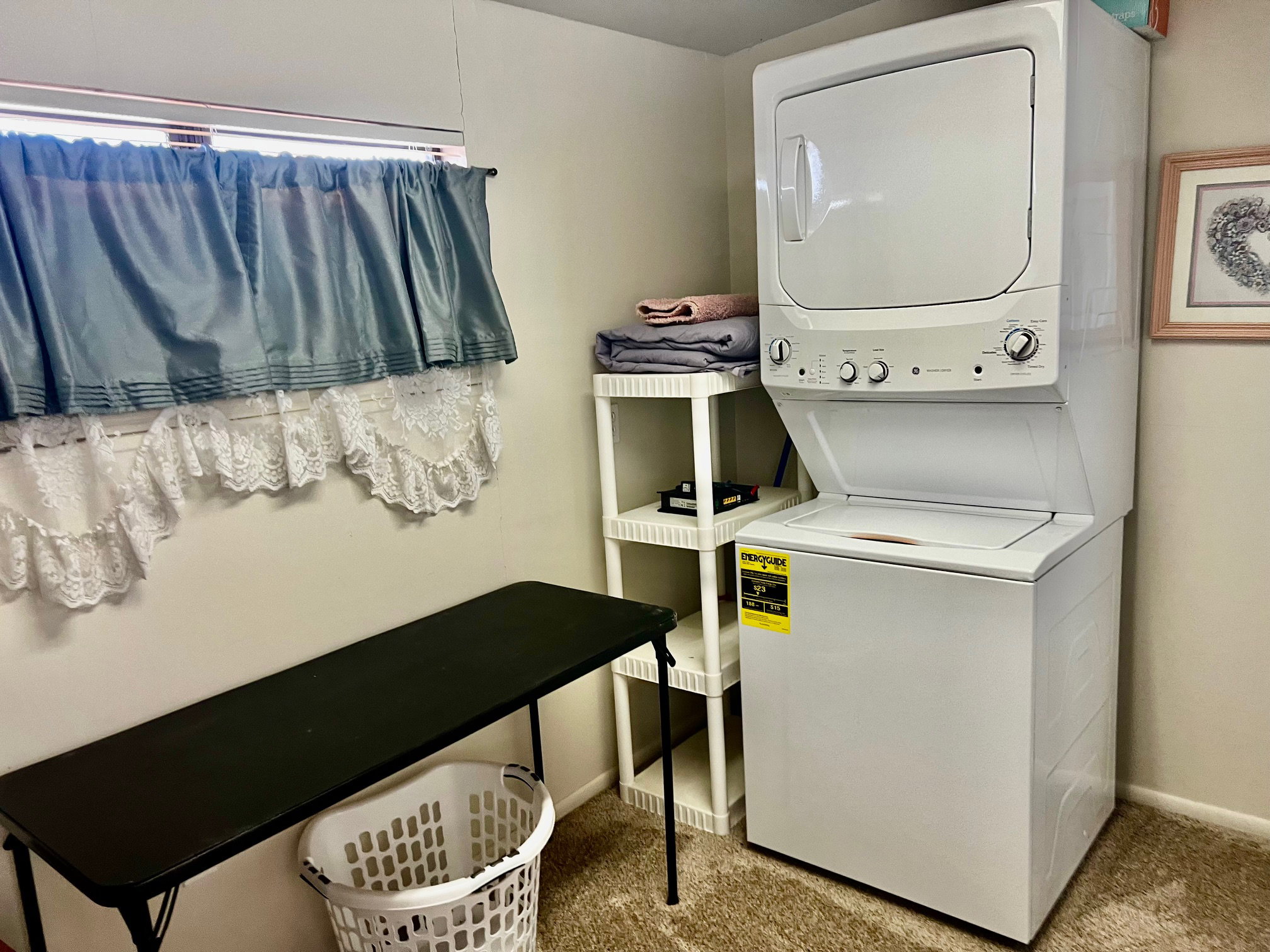 Laundry area with light colored carpet and stacked washing machine and dryer