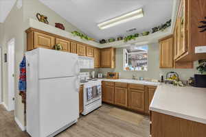 Kitchen with white appliances, brown cabinets, light countertops, vaulted ceiling, and light wood-style flooring