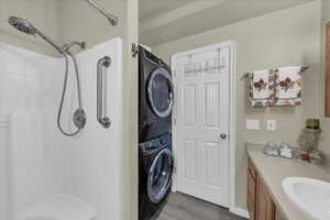 Bathroom featuring vanity, stacked washing machine and dryer, light wood-style floors, and a shower stall