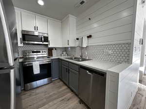 Kitchen with stainless steel appliances, white cabinetry, gray cabinetry, light wood-style floors, and recessed lighting