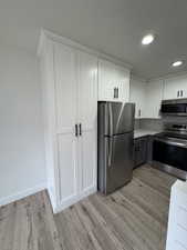 Kitchen with white cabinetry, appliances with stainless steel finishes, gray cabinetry, decorative backsplash, and light wood-style floors