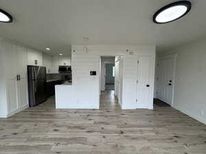Family room/ Kitchen featuring white cabinetry, light wood-style floors, appliances with stainless steel finishes, and light countertops. Walls have board and batt details