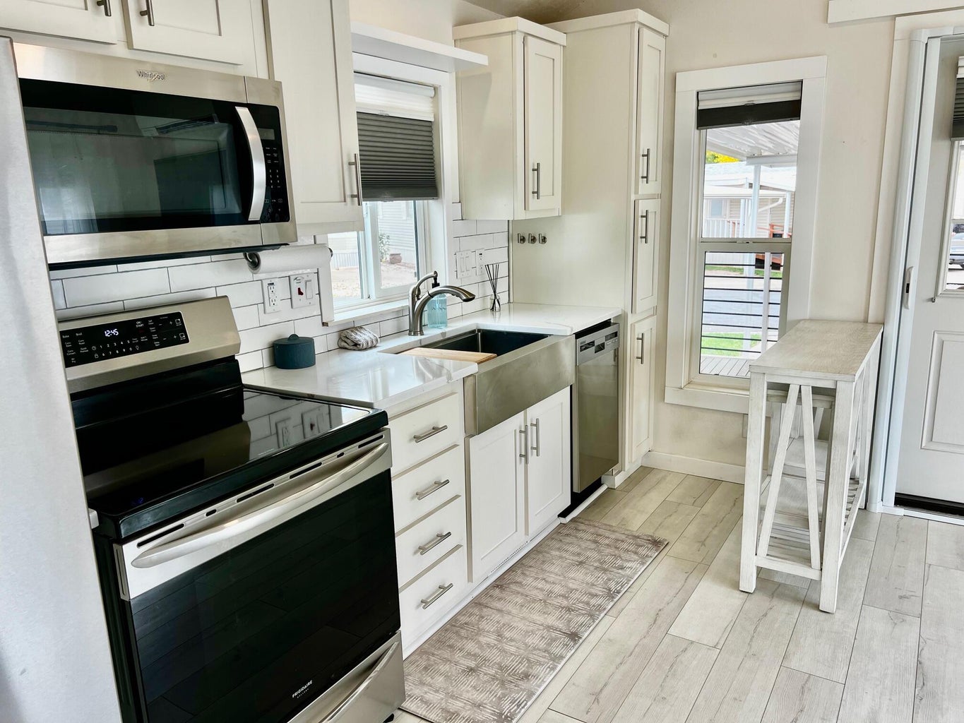 Kitchen featuring stainless steel appliances, tasteful backsplash, white cabinetry, light wood-style flooring, and light stone counters