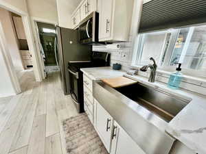 Kitchen with white cabinets, electric range, light stone counters, backsplash, and stainless steel microwave