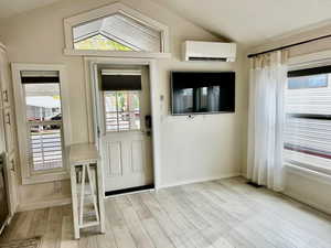 Foyer entrance featuring vaulted ceiling, an AC wall unit, and light wood finished floors