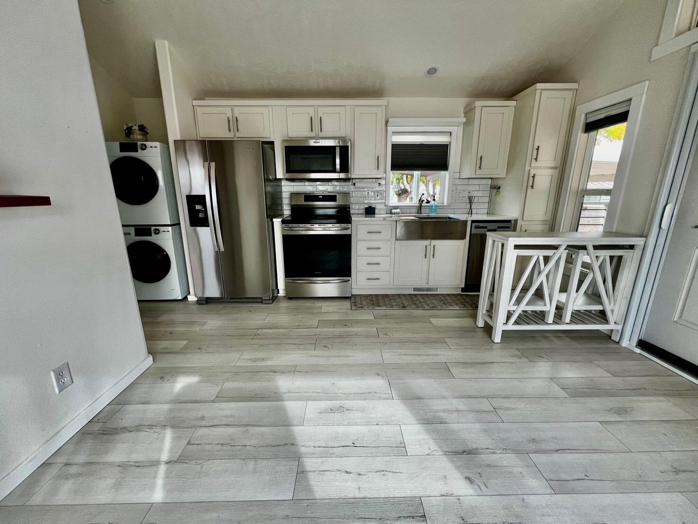 Kitchen with appliances with stainless steel finishes, backsplash, white cabinets, light wood-style floors, and estacked washer and dryer