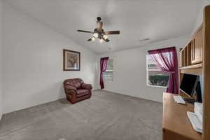 Unfurnished room featuring vaulted ceiling, light colored carpet, a ceiling fan, and a desk