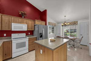 Kitchen with white appliances, lofted ceiling, light tile patterned floors, a kitchen island, and a chandelier