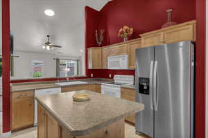 Kitchen with white appliances, light brown cabinetry, lofted ceiling, a kitchen island, and recessed lighting