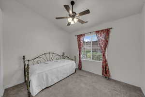 Carpeted bedroom featuring lofted ceiling and a ceiling fan