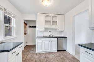 Kitchen with dark countertops, white cabinetry, backsplash, and stainless steel dishwasher