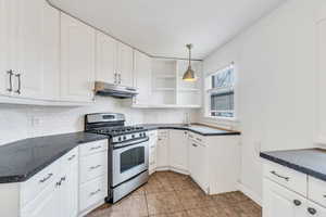 Kitchen featuring dark countertops, gas range, decorative light fixtures, and white cabinets