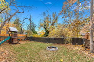 Fenced backyard featuring a fire pit and a playground