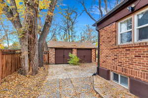 View of property exterior featuring an outdoor structure, brick siding, a detached garage, and a fenced backyard