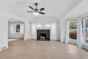 Unfurnished living room featuring vaulted ceiling, light wood finished floors, arched walkways, a brick fireplace, and a ceiling fan