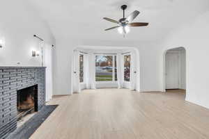 Unfurnished living room with vaulted ceiling, light wood-type flooring, arched walkways, a brick fireplace, and ceiling fan