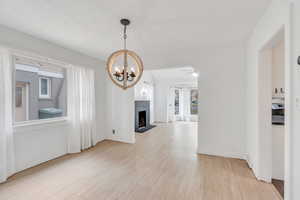 Unfurnished dining area with a fireplace, light wood finished floors, a chandelier, arched walkways, and a ceiling fan