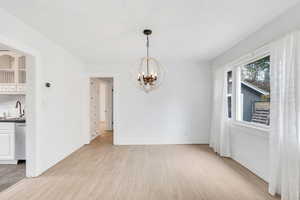 Unfurnished dining area featuring light wood-type flooring and a chandelier