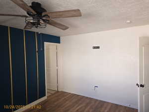 Empty room with a textured ceiling, wood finished floors, and ceiling fan